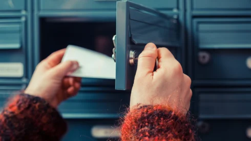 Hands open a mail box and pulls out a piece of direct mail marketing
