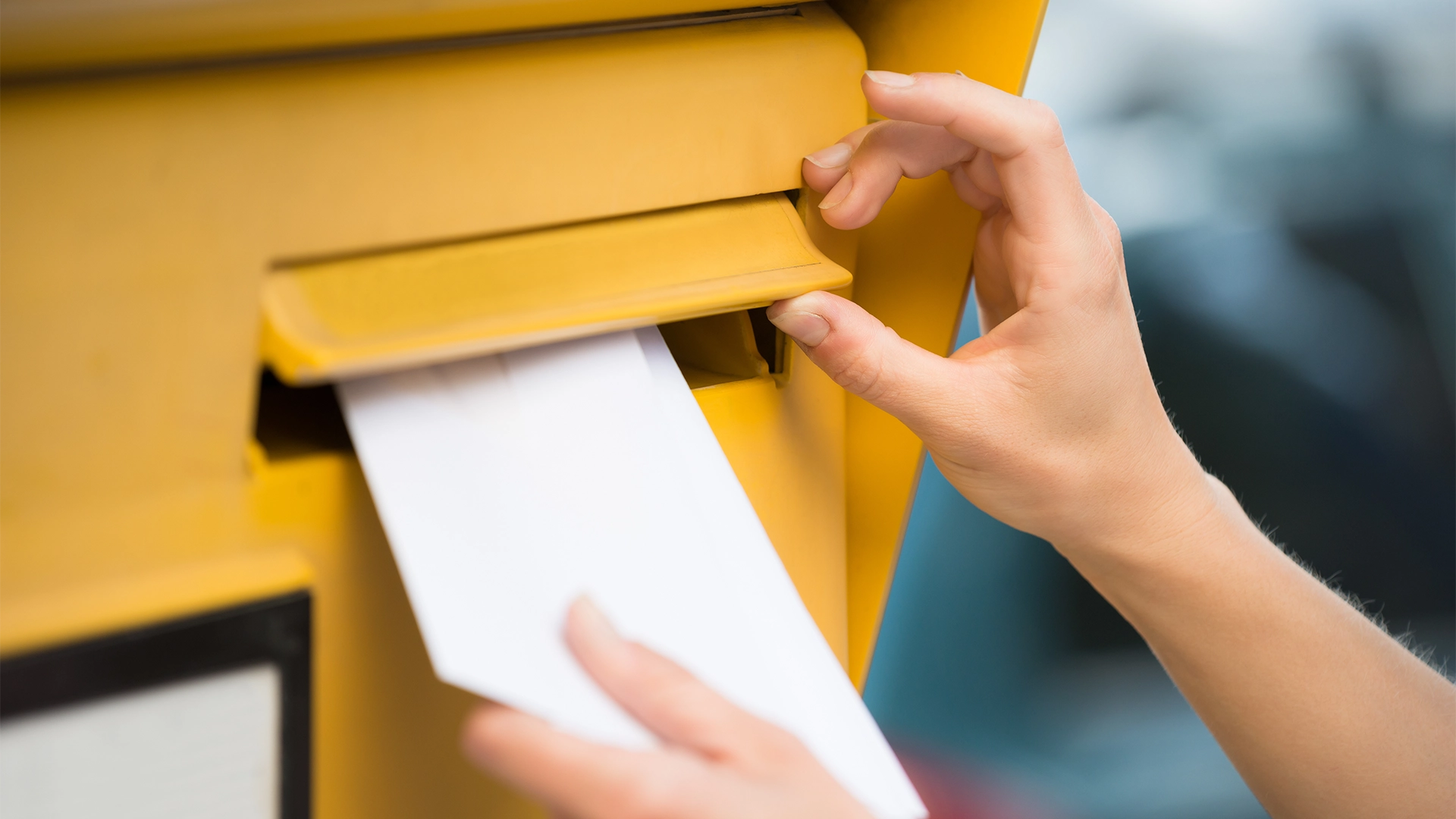 Image of letter being posted into yellow postbox.