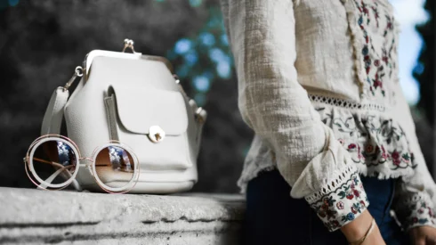A fashion retailer marketing campaign image shows a person sitting on a wall with a handbag and sunglasses next to them