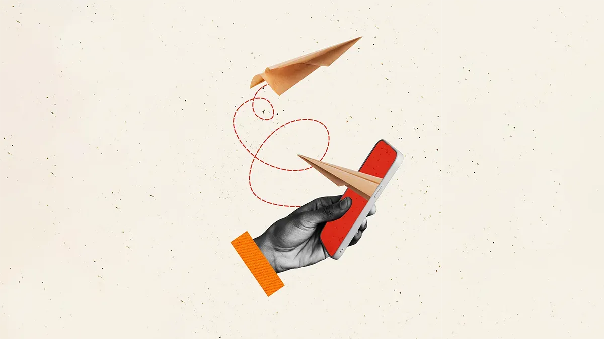 a hand holds a mobile phone as paper planes representing door drop mail fly out of the screen