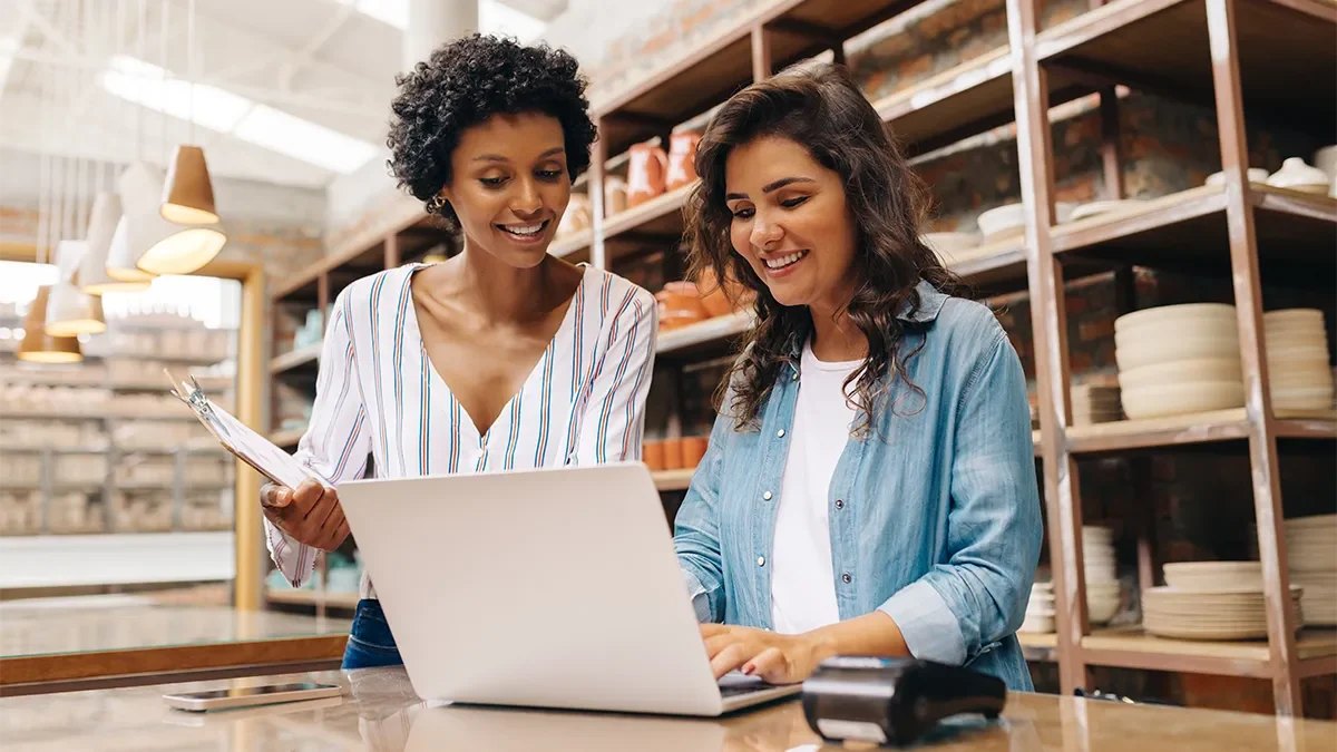Two business owners smile at their laptop as they process orders for their new online ecommerce site.